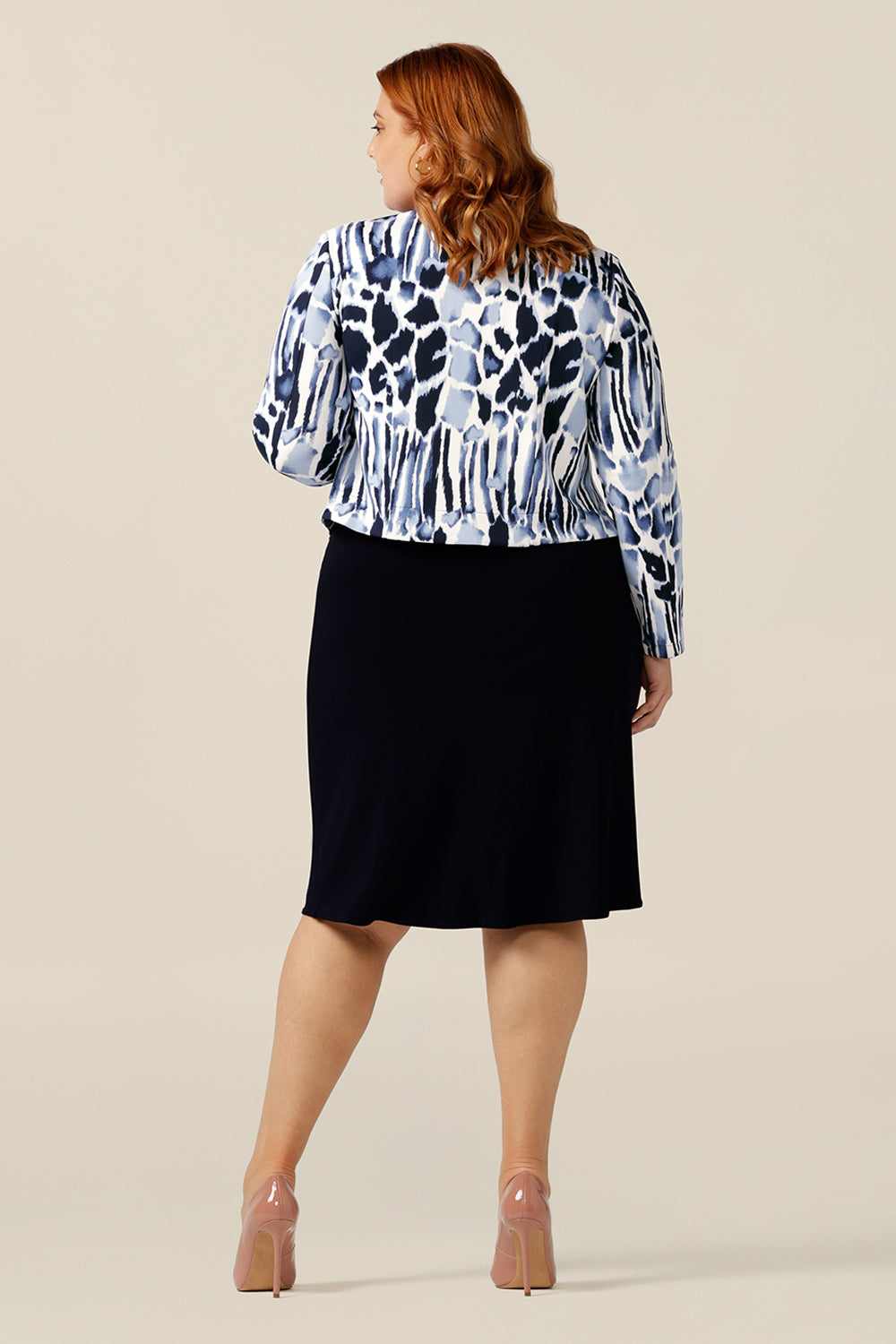 A size 18, plus size woman wears a collarless open front jacket with long sleeves. In navy and white jersey, this corporate jacket is comfortable office wear. Designed with the women of Australia and New Zealand in mind, this quality work wear jacket is made in sizes 8 to 24.